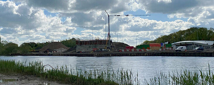 foto van het bouwterrein vanaf de overkant van het kanaal
